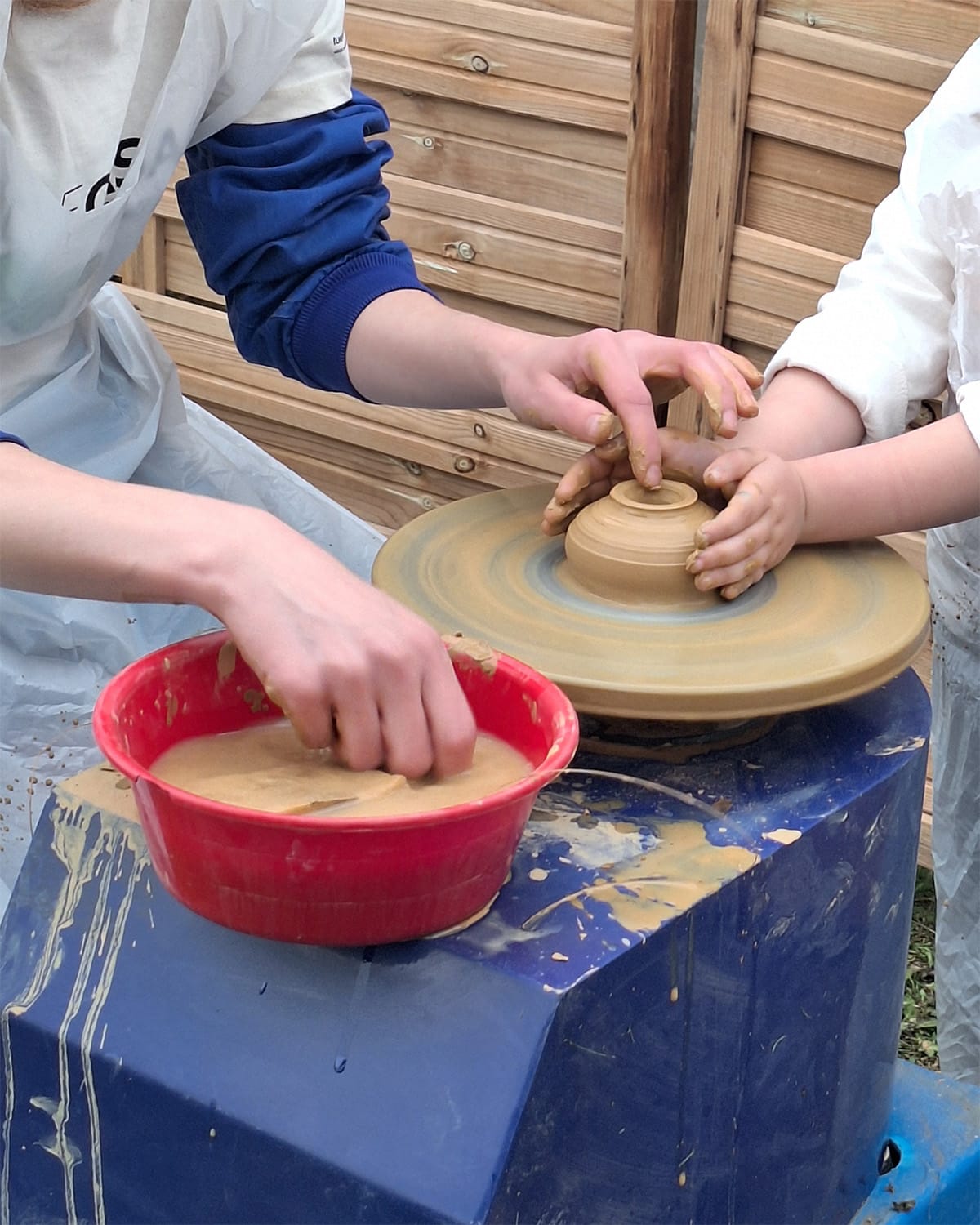 A kid experiments throwing a pot with the help of an artisan at Legado Artesano.